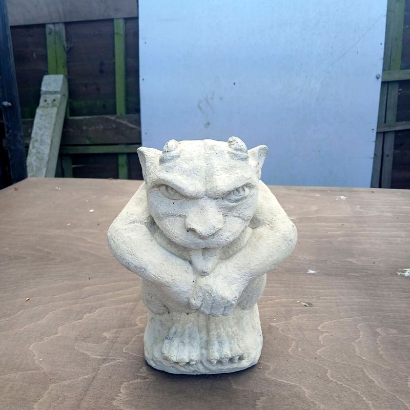Small gargoyle with horns, crouching with its tongue out, in pale stone